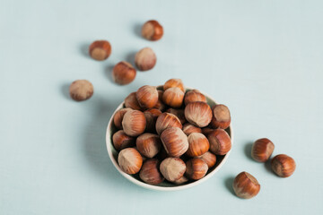 Pile of hazelnuts filbert in a bowl on a light blue background