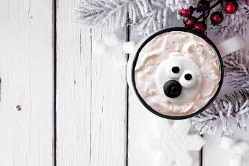 Fotobehang Hot chocolate with polar bear marshmallows. Above view table scene with Christmas corner border against a white wood background. Copy space. © Jenifoto