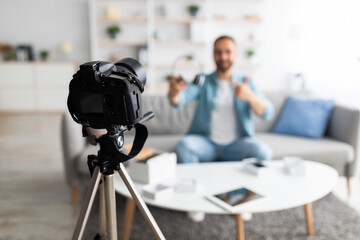 Video blogger recording review of wireless headphones at home, selective focus on modern dslr camera