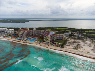 Fototapeta premium Aerial photograph. The resort town, many high-rise buildings, hotels, swimming pools. Sandy shore. The sea near the coast is polluted with algae. Environmental protection.