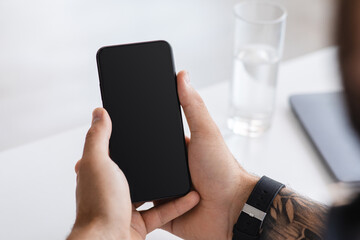Modern young european male blogger typing on phone with blank screen, chatting on social networks