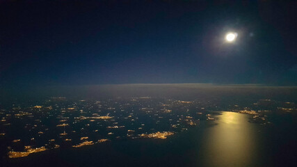 Landschaftsfoto bei Nacht aus dem Flugzeug aufgenommen mit Horizont und Mond und den vielen Lichtern der beleuchteten Ortschaften und St&auml;dte  
