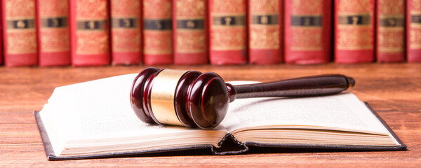 Legal Law and Justice concept - Open law book with a wooden judges gavel on table in a courtroom or...