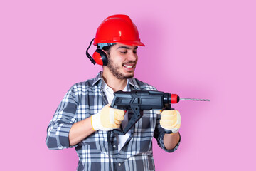 Young builder with a drill puncher, isolated on pink background..