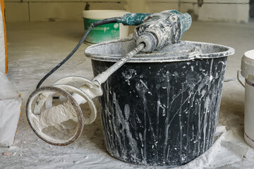 On a dirty black plastic bucket lies a punching machine with a nozzle for mixing dry mixes....