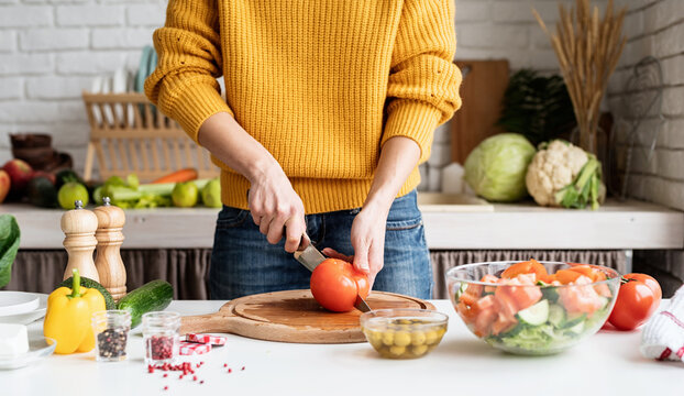 Front view of female hands making salad cutting tomatoes in the kitchen