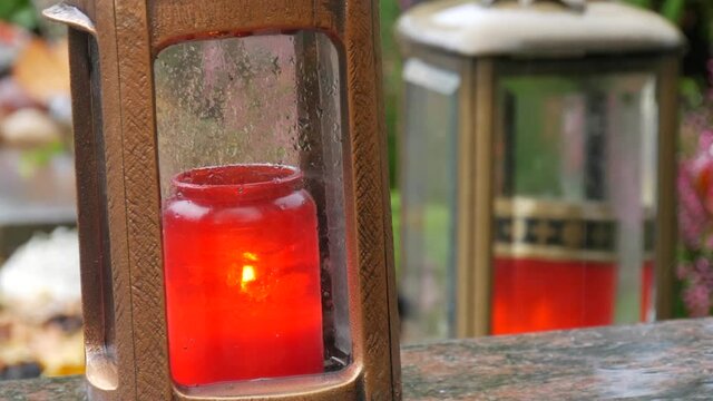 Red memorial candle burning with fire on rainy day on tombstone in cemetery autumn, rainy day. Grave with tombstone on which raindrops falling, against abackground of yellow foliage. Day of all dead