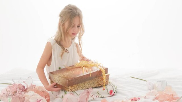 A little girl opens a box with a bright light and rejoices at the gift she sees. Child in the studio on a white background.