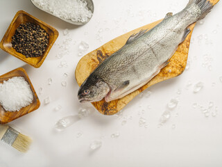 Fresh fish on a cutting wooden board, salt, pepper and spices in wooden bowls. White background,...