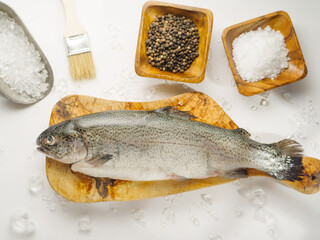 One fresh fish on a cutting board, spices, salt, brush. Large group of objects. White background, high angle view. Fish and seafood dishes, advertising, fishing, fish market, restaurant, recipe book.