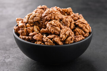 Peeled walnuts in a bowl on a black textured background, side view.
