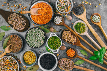 a large selection of spoons and bowls with various legumes on a wooden background. - obrazy, fototapety, plakaty