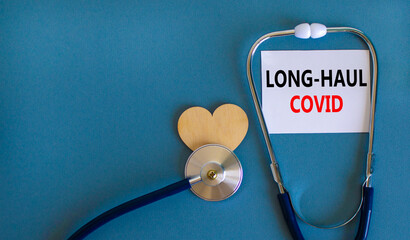 COVID-19 long-haul covid symptoms symbol. White card with words long-haul covid. Wooden heart, stethoscope, beautiful blue background, copy space. Medical, COVID-19 long-haul covid symptoms concept.