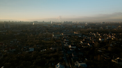 The suburb is backlit by the setting sun. Houses, a park area and a city highway are visible. Aerial photography.