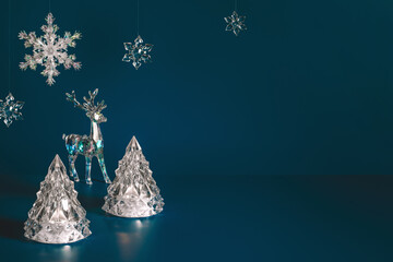  Winter scene with Christmas decorations made of crystal glass. Xmas trees, deer and snowflakes on dark blue background with copy space, front view.