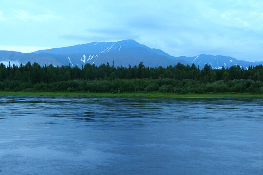 View of a calm wide river with mountains in the background in a blue fog scenic image of the northern wilderness of Russia