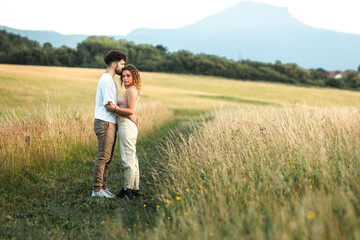Naklejka na ściany i meble Lovely heterosexual couple in a grass field walking and kissing