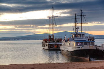 Pleasure ships are moored in Gelendzhik Bay at sunset. Dramatic sunset sky, sandy beach.