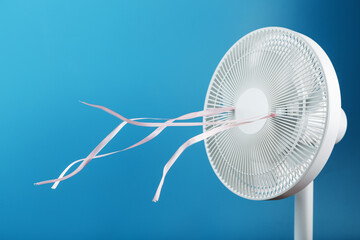 The electric fan is white with pink ribbons fluttering in the wind on a blue background - obrazy, fototapety, plakaty