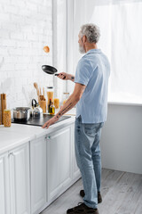 Mature man throwing pancake and holding frying pan in kitchen.