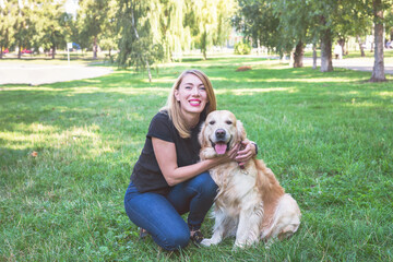 Young woman hugs her retriever while sitting on the grass