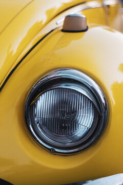 Headlight Close Up Shot Of Yellow Colored Volkswagen Brand And German Product Car On The Street.