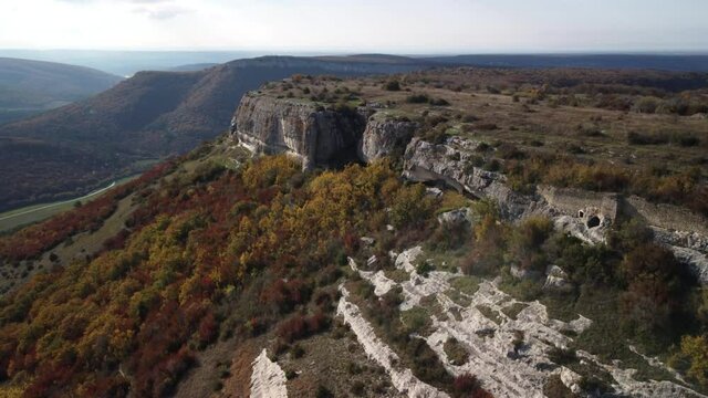 Flying over the cliff in the Mangup gorge. The edge of the white cliff rises above the bright trees. Bright colors of the Crimean autumn. 4k drone video