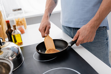 Cropped view of man with spatula cooking pancake in kitchen.