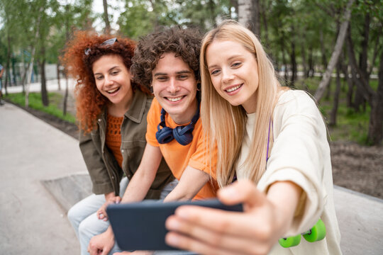 smiling blonde woman taking selfie with happy friends in park.