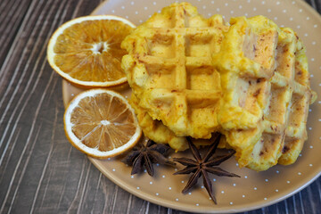 Belgian gluten-free pumpkin waffles lie on a brown plate with a dry slice of lemon and anise stars on a wooden table. side view. gluten-free