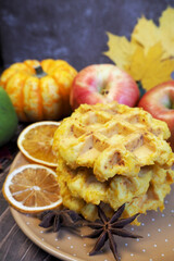 Belgian gluten-free pumpkin waffles lie on a brown plate with a dry slice of lemon and stars of anise, pumpkin, apples against a background of yellow maple leaves on a wooden table. side view. gluten-