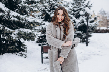 Fototapeta na wymiar Girl walking in a snowy park laughing and wearing a coat