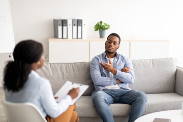 Obraz premium Psychologist helping black male patient, working with unhappy African American man, providing support at clinic