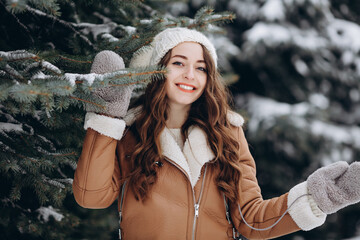 Portrait of happy girl in a winter park wearing a jacket and bright jeans and mittens and a hat looking at camera