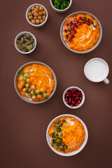 Pumpkin puree soup of butternut squash in bowls with chickpeas and green onions, pumpkin and pomegranate seeds, top view on plates with food on brown background