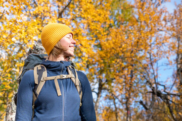 Caucasian Female Hiker Hiking Kings Trail with Intense Yellow Autumn Birch Tree Foliage Background Outdoor Looking Happy Smiling to camera and enjoying the Sunlight in Pieljekaise National park.