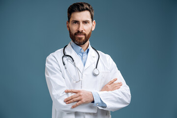 Portrait photo of friendly family doc man wearing white lab coat and stethoscope smiling reliable and standing arms crossed at the empty area isolated blue color background