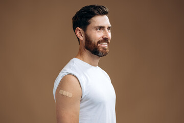 Obraz premium Man receives covid 19 vaccine injection. Young caucasian man with adhesive plaster bandage at his arm with after getting vaccinated for coronavirus. Vaccination concept