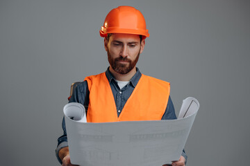 Confident caucasian man wearing helmet holding tube with drawings standing at the studio over the gray wall and examining blueprints. Engineer man concept