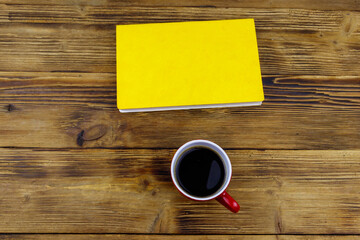 Cup of coffee and book on wooden table. Top view
