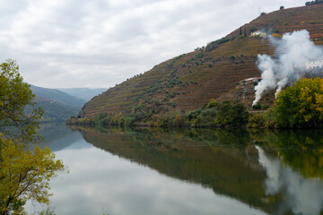View on Douro river with reflection in water of colorful hilly stair step terraced vineyards in autumn, wine making industry in Portugal