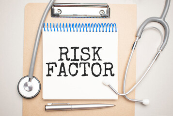 White notepad with the words risk factor and a stethoscope on a blue background. Medical concept