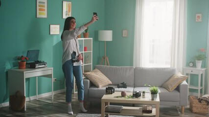 Young woman, blogger, influencer, is staying at home, recording home video on her smartphone to show her everyday life routine to subscribers, happy and inspired, Slow motion.