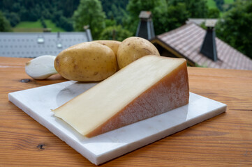 Tastes of Savoia, French cow cheese for gratin abondance, potatoes and french mountains village in Haute-Savoie on background