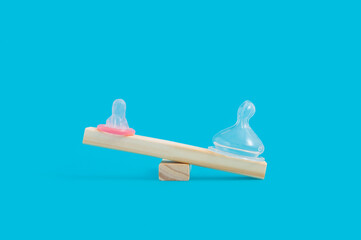 Minimal pregnancy concept with condom and silicone pacifier on wooden seesaw
