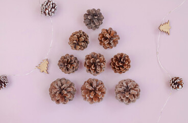 Christmas tree made of pine cones and wooden decorations on pastel pink background, top view. 