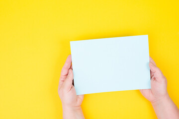 Holding empty paper in the hands, yellow colored background, copy space for text, blank card