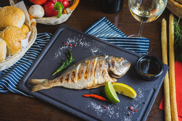 Grilled fish on a plate with a glass of wine and baked vegetables.