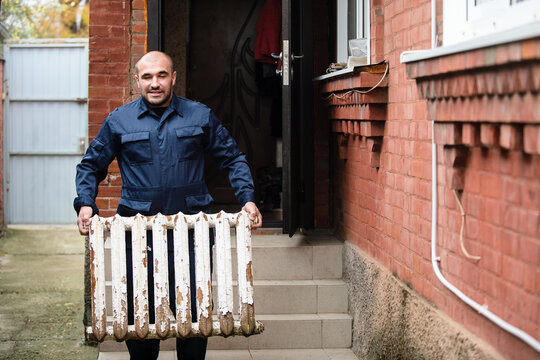 A man changes the heating in the house, takes out old peeled cast-iron radiators. The concept of modern heating, replacement of the old with a new one. Warmth in the house