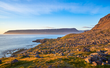A scenic coastal landscape featuring a rocky shoreline and a calm sea. The serene atmosphere and the natural beauty of the coastline are captured in this picturesque setting.